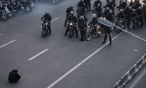 Moment an Iranian protester sits in the road, blocking a police convoy