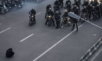 Moment an Iranian protester sits in the road, blocking a police convoy
