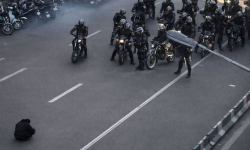 Moment an Iranian protester sits in the road, blocking a police convoy