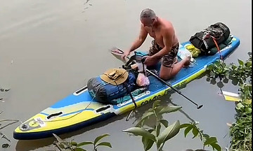 Western tourist paddleboards on river, welcomed by entire Mekong Delta hamlet